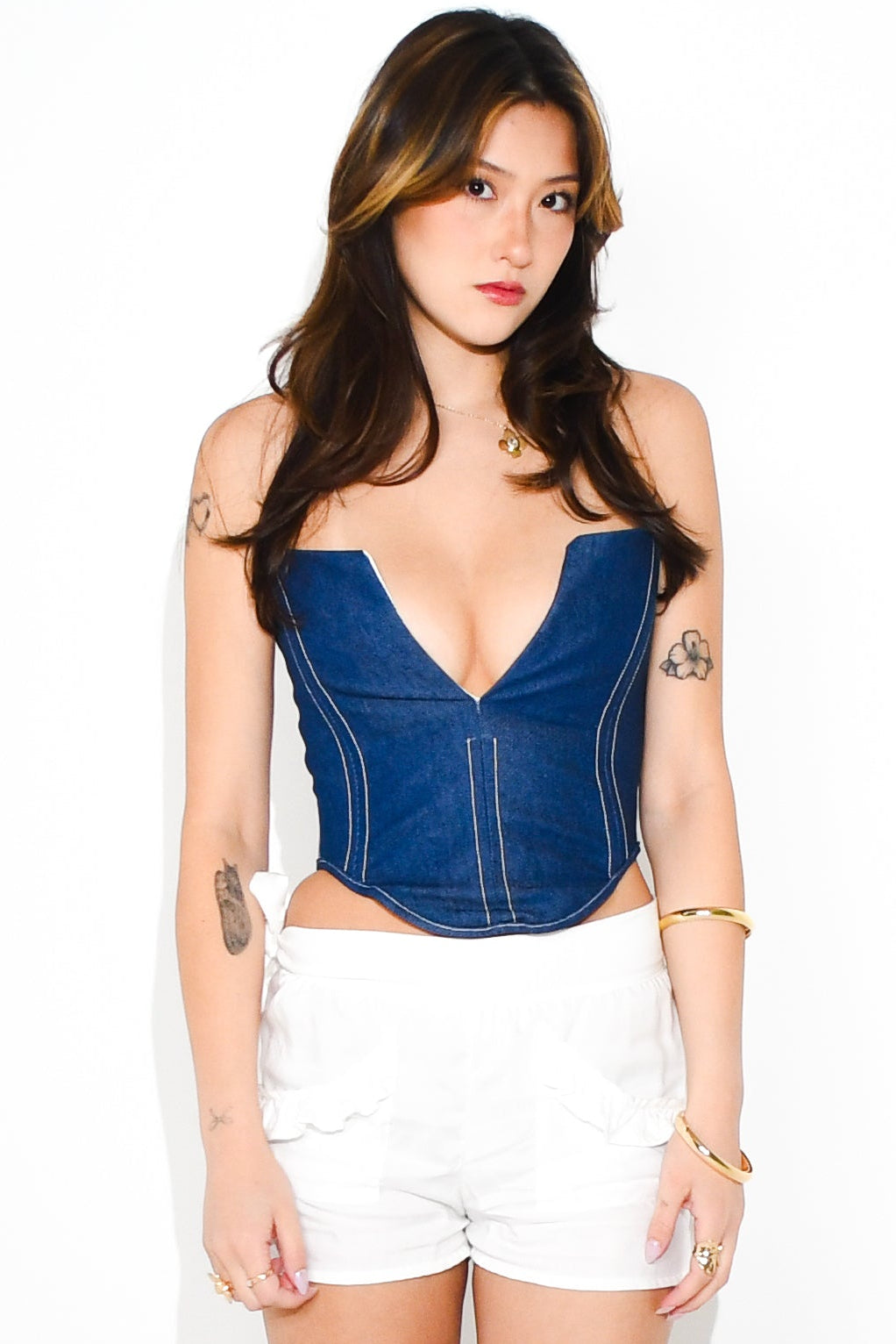 Woman wearing a blue denim corset, white shorts, and black high-heeled boots on a white background